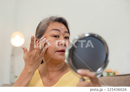 Beauty and Skincare Routine. A senior woman applying cream to her face while looking in the mirror. Beauty and Skincare Routine. A senior woman applying cream to her face while looking in the mirror. 125436026