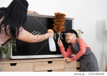 Home Cleaning and Family Bonding. A child helping his mother clean the living room with a duster and vacuum. Home Cleaning and Family Bonding. A child helping his mother clean the living room with a duster and vacuum. 125436059
