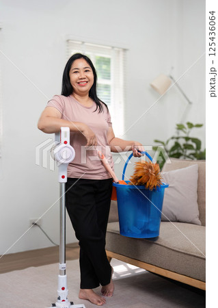 Home Cleaning and Maintenance. A woman standing with cleaning supplies, ready to clean her living space. Home Cleaning and Maintenance. A woman standing with cleaning supplies, ready to clean her living space. 125436064