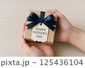 父の日ギフトを包む両手・クラフト包装とネイビーリボン 125436104