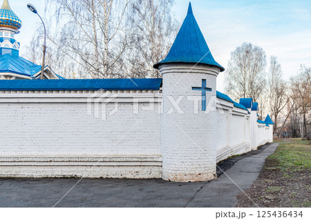 White brick monastery wall with blue-roofed towers and blue cross, with bare trees and clear sky, symbolizing religion White brick monastery wall with blue-roofed towers and blue cross, with bare trees and clear sky, symbolizing religion 125436434