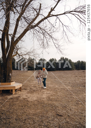 A man swings a girl on a swing in a field. A man swings a girl on a swing in a field. 125437656