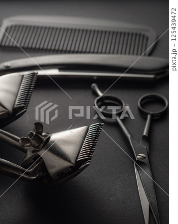 Various classic barber tools are displayed on a black background, highlighting an array of equipment including clippers, scissors, and a comb, used for grooming. 125439472