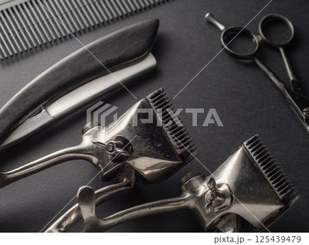 Antique barber tools are artfully placed on a dark surface, highlighting scissors, clippers, and a comb. This setup reflects the classic aspect of grooming and hairstyling. 125439479