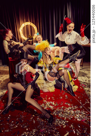 Elegant cabaret women in vintage posing with drinks, cigarettes and laughter on red carpet surrounded by confetti. 125440086