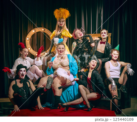 Cabaret ensemble sitting in layers striking joyful pose on red carpet with glamorous retro energy. Men and women with bold makeup. Cabaret ensemble sitting in layers striking joyful pose on red carpet with glamorous retro energy. Men and women with bold makeup. 125440109