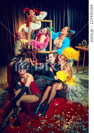 Cabaret group of men and women posing with golden frame in vintage circus mood on red floor with theatrical outfits. 125440169