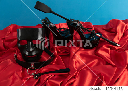 Adult sex games. Kinky lifestyle. Spank and a pair of black high-heeled shoes on the red linen. Bdsm outfit 125441584