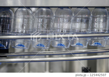 The empty drinking water bottles hanging on the overhead conveyor belt for filling process. The empty drinking water bottles hanging on the overhead conveyor belt for filling process. 125442507
