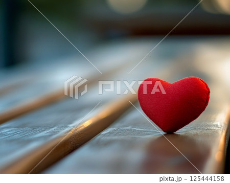A shiny red heart-shaped object lies on a textured wooden surface, reflecting light and symbolizing love, emotion, and craftsmanship. 125444158