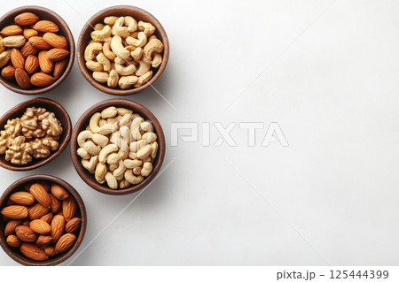 A variety of nuts and dried fruits arranged in wooden bowls on a light gray surface, showcasing a nutritious and colorful selection of healthy snacks. 125444399