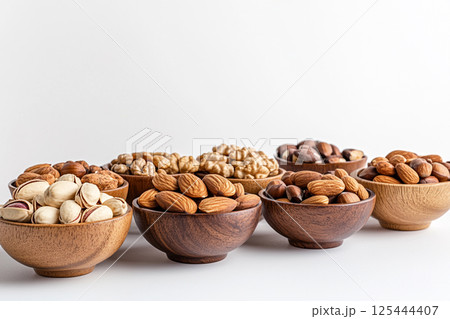 A variety of nuts and dried fruits arranged in wooden bowls on a light gray surface, showcasing a nutritious and colorful selection of healthy snacks. A variety of nuts and dried fruits arranged in wooden bowls on a light gray surface, showcasing a nutritious and colorful selection of healthy snacks. 125444407