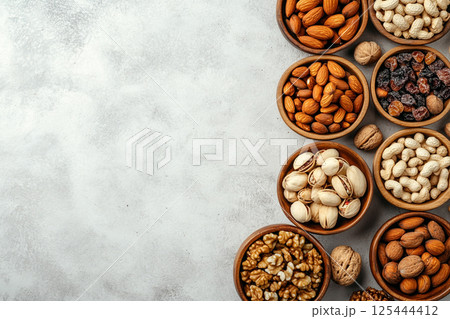 A variety of nuts and dried fruits arranged in wooden bowls on a light gray surface, showcasing a nutritious and colorful selection of healthy snacks. 125444412