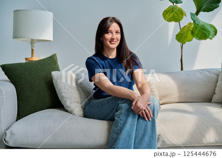 Portrait of beautiful young brunette woman sitting on sofa in living room Portrait of beautiful young brunette woman sitting on sofa in living room 125444676