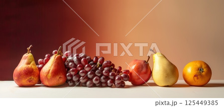 Fresh fruit, pears, grapes, and an orange on a white table, with a blurred orange and red background. 125449385
