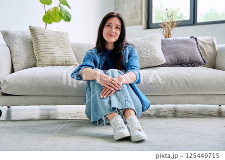 Portrait of beautiful young brunette woman sitting on sofa in living room Portrait of beautiful young brunette woman sitting on sofa in living room 125449715
