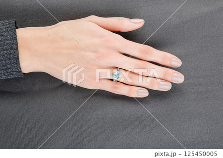 Beautiful female hand with gold ring with diamonds and aquamarine on gray background Beautiful female hand with gold ring with diamonds and aquamarine on gray background 125450005