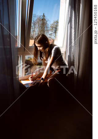 Creative child immersed in drawing sitting by window at home. Drawing hobby for developing imagination and motor skills. Creative education and kids activities concept. Creative child immersed in drawing sitting by window at home. Drawing hobby for developing imagination and motor skills. Creative education and kids activities concept. 125450168