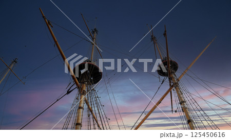 Old sailing ship masts reaching towards the twilight sky with vibrant colors illuminating the horizon Old sailing ship masts reaching towards the twilight sky with vibrant colors illuminating the horizon 125450616
