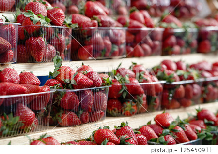 Close-up of ripe strawberries for sale on market stall. Fresh strawberries in plastic cups displayed at a street market stall 125450911