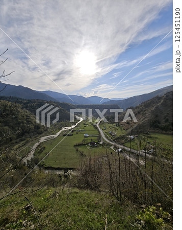 Breathtaking mountain valley landscape with winding river and road under cloudy sky Breathtaking mountain valley landscape with winding river and road under cloudy sky 125451190