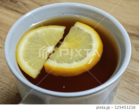 Two lemon slices floating in a cup of black tea on wooden table 125451216