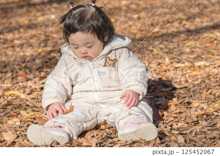 【落ち葉で敷き詰められた冬の公園で遊ぶ1歳児　座る】 125452067