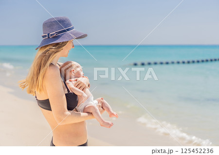 Mother holding her newborn baby by the turquoise sea, sharing a peaceful and loving moment. Family bonding, motherhood, and travel with baby concept Mother holding her newborn baby by the turquoise sea, sharing a peaceful and loving moment. Family bonding, motherhood, and travel with baby concept 125452236
