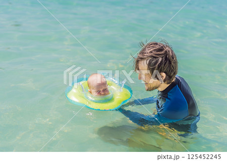 Father and newborn son swimming in the turquoise sea. Baby floating in an inflatable neck ring. Family bonding, fatherhood, and baby first water experience concept Father and newborn son swimming in the turquoise sea. Baby floating in an inflatable neck ring. Family bonding, fatherhood, and baby first water experience concept 125452245