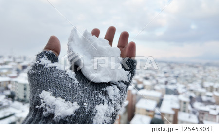 Snow gently sits on a hand overlooking a snowy cityscape 125453031