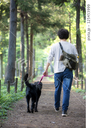緑の多い田舎道で散歩を楽しむ男性と大型犬 緑の多い田舎道で散歩を楽しむ男性と大型犬 125453999