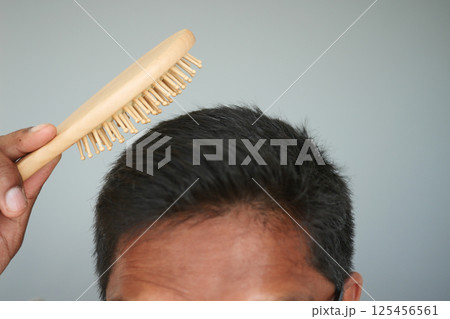 Man grooming his hair with a wooden brush at home Man grooming his hair with a wooden brush at home 125456561