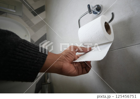 Hand reaching for toilet paper in modern bathroom setting Hand reaching for toilet paper in modern bathroom setting 125456751