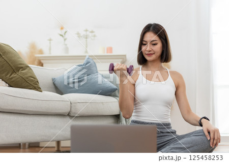 young female working out shoulder holding up dumbbell active strong exercising arm training online looking laptop muscle fitness weight. 125458253