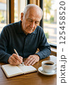 カフェでノートを書くシニア男性の手元 125458520