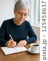 カフェでノートに文字を書くシニア女性の手元とコーヒー 125458637