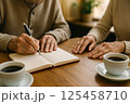 カフェでノートを囲むシニア夫婦の手元とコーヒー 125458710