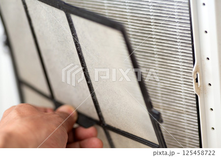 空気清浄機の汚れたフィルターを掃除する手元 125458722