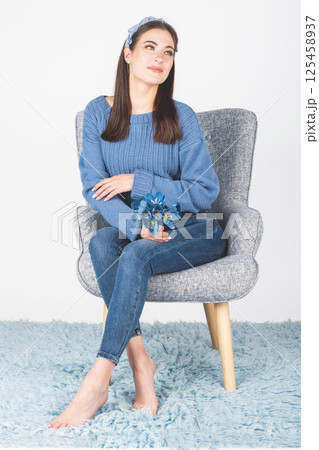 Woman with sweater, jeans and flowers sitting on armchair Woman with sweater, jeans and flowers sitting on armchair 125458937