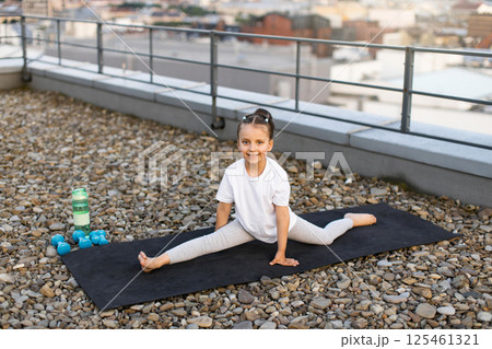 Child practicing yoga posture outdoors on rooftop. Female, approximately 8 years old, showing healthy activity, fitness lifestyle, focus on stretching and flexibility development. Child practicing yoga posture outdoors on rooftop. Female, approximately 8 years old, showing healthy activity, fitness lifestyle, focus on stretching and flexibility development. 125461321