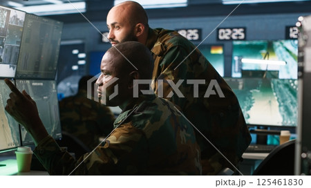 Air force officers performing tactical level reconnaissance in command post, looking at monitors. Military soldiers using radar devices to look at assault zones on displays, camera A 125461830