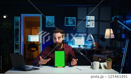 Tech specialist presenting chroma key tablet in entry level low budget price range to interested viewers, filming in studio. Viral content creator reviewing green screen digital device, camera B 125461891