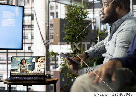 African american manager holding online video conference meeting with remotely working workers. Teleworking executive in stylish office discussing with employees during video call 125461946