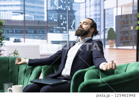 Businessman in a modern office unwinds with meditation music, finding harmony and calmness in his busy schedule. CEO with a relaxed posture highlights the importance of self care. 125461948