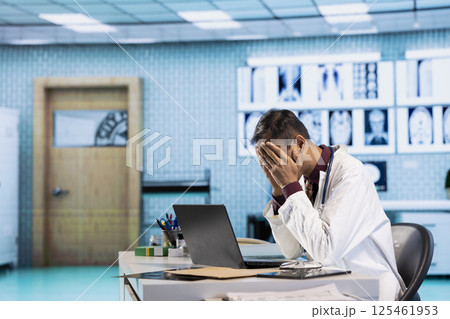 Stressed physician working late at night under pressure fighting to find a cure for a patient with dangerous disease, healthcare services. Overworked unhappy medic with anxiety at hospital. 125461953