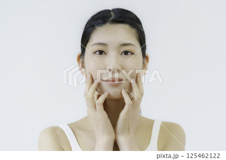 白背景の頬に手を当てる若い女性の顔のアップ 125462122