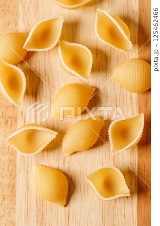 Raw uncooked dried Conchiglie shell pasta. Italian seashells pasta on wooden background. 125462466