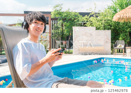 プールサイドでリクライニングチェアに座りゲームをする若いアジア人男性 125462978