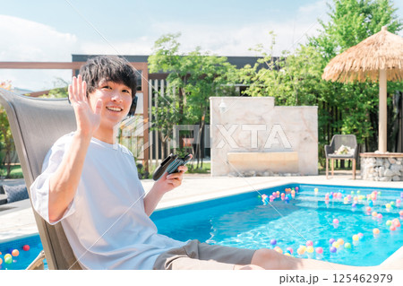 プールサイドでリクライニングチェアに座りゲームをする若いアジア人男性 125462979