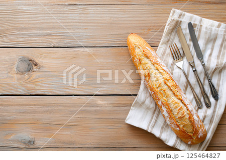 A golden crusted rustic French baguette rests on a wooden table with vintage cutlery A golden crusted rustic French baguette rests on a wooden table with vintage cutlery 125464827